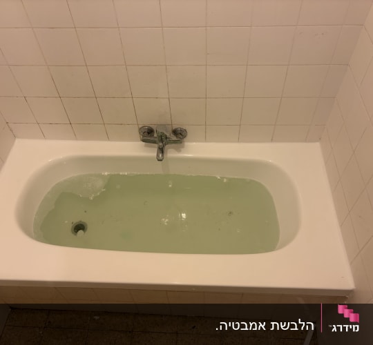 אמבטיה עם מים ירקרקים על רקע קיר מרוצף